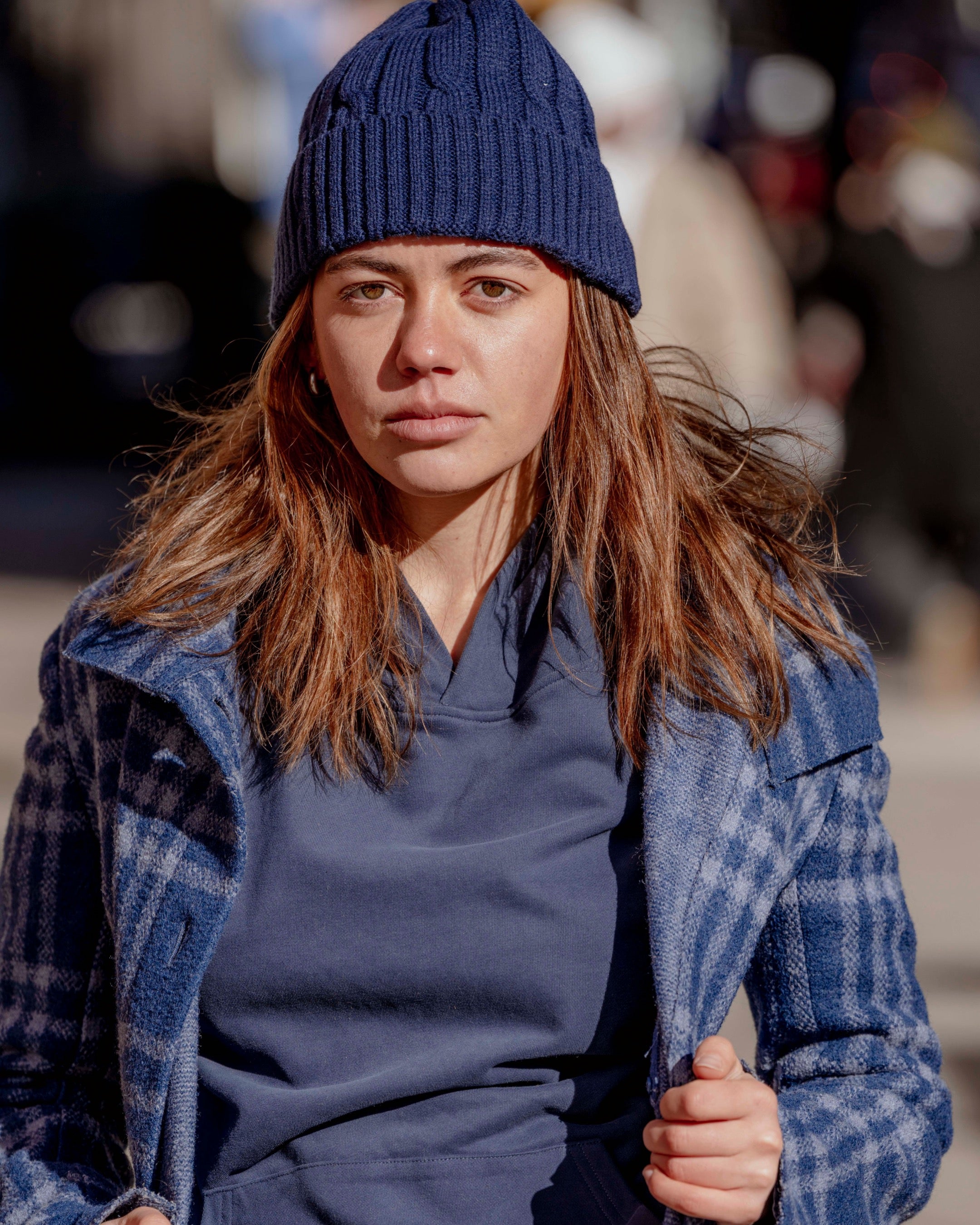 Woman wearing a blue knit hat and plaid coat in an urban setting