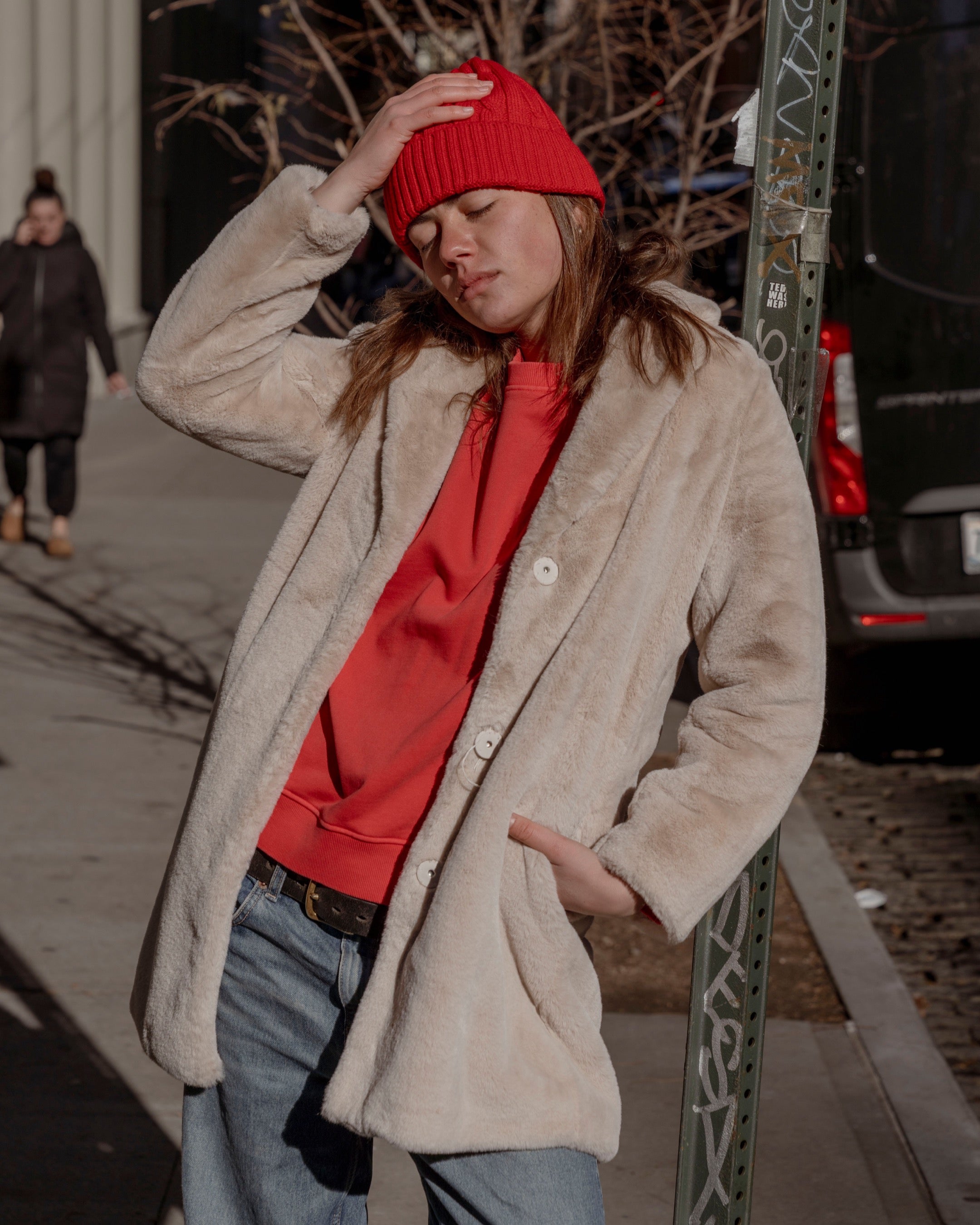 Person wearing a red beanie and beige coat on a city street.