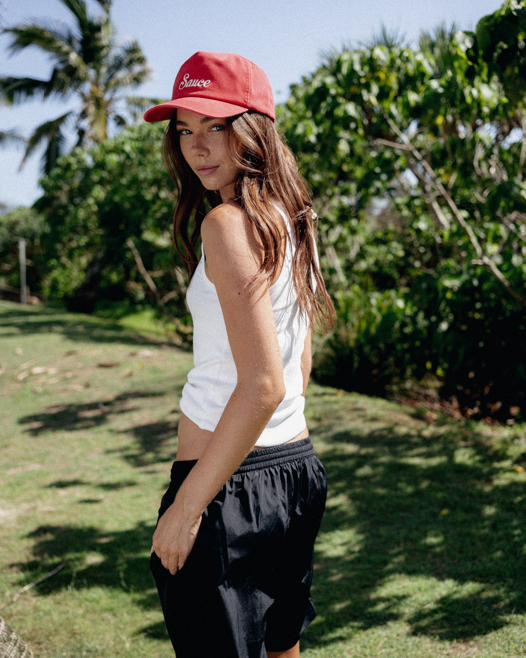 Woman wearing a red cap and white tank top in a natural setting