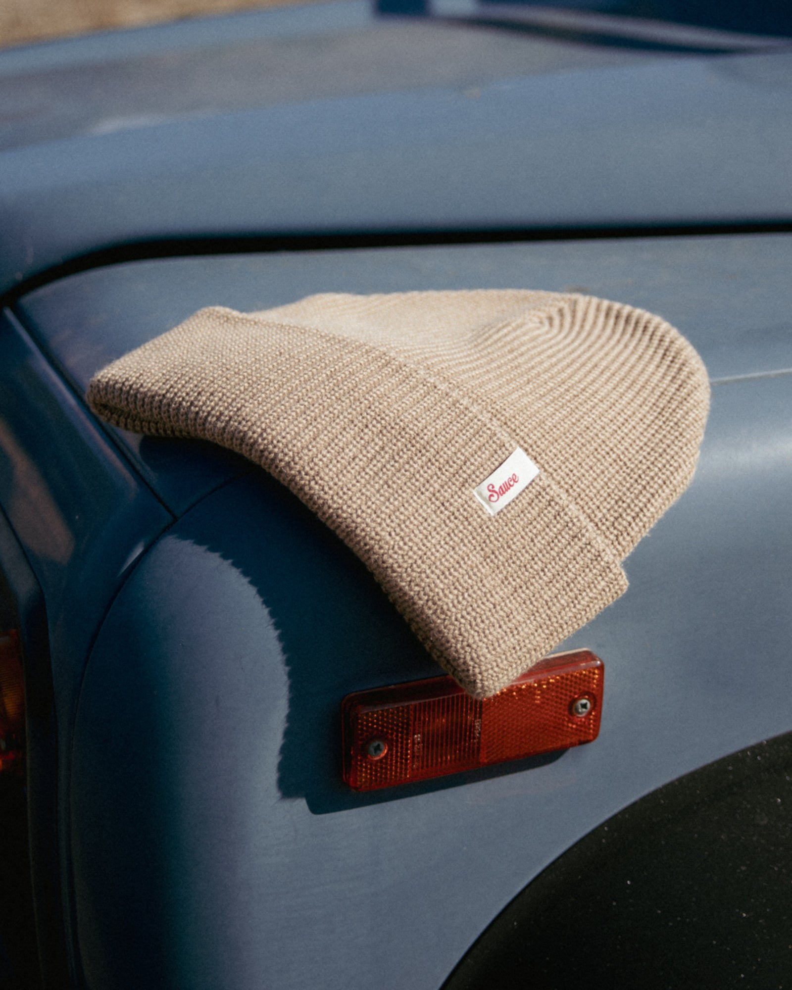 Beige knit beanie with a logo on a car's hood