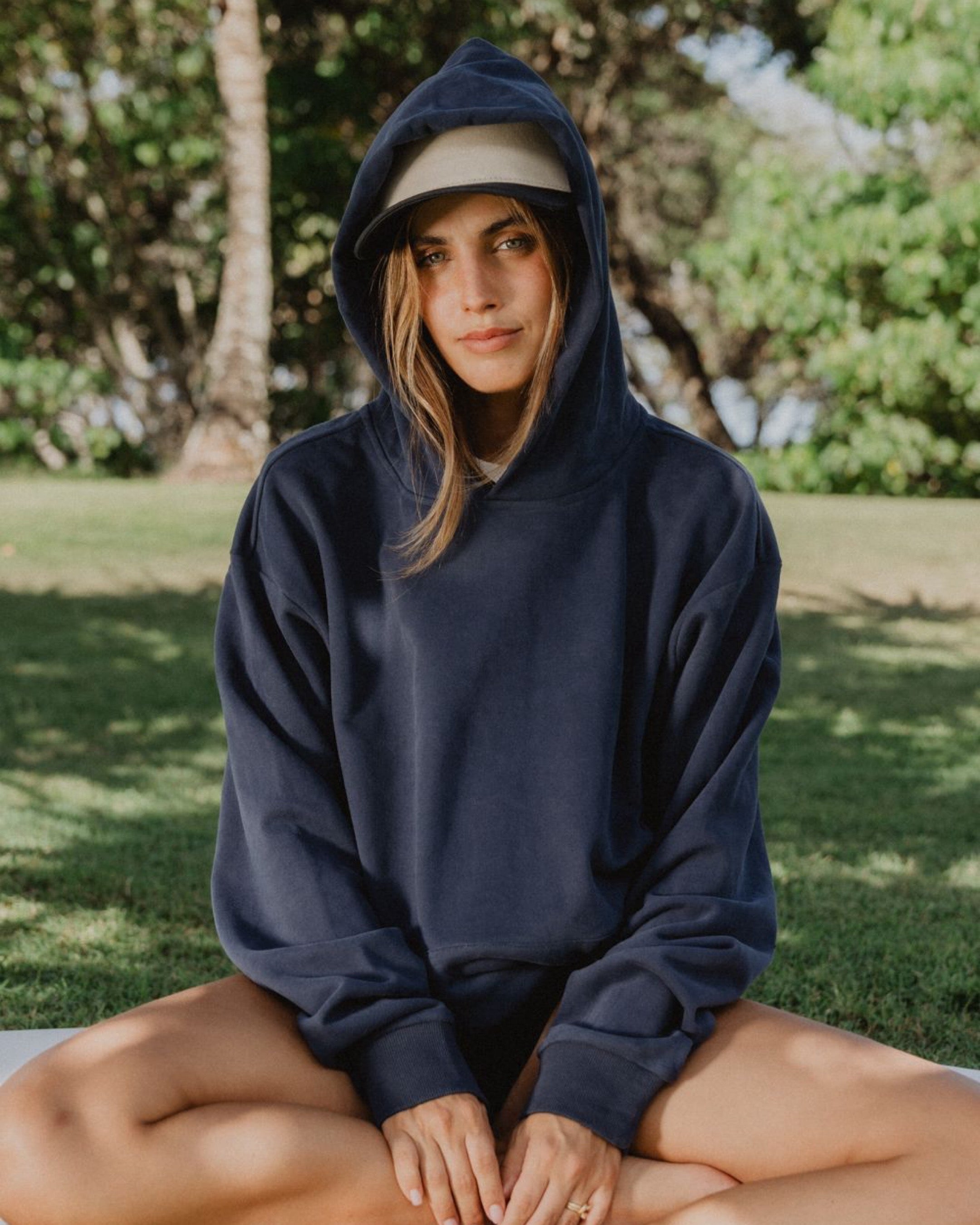 Person wearing a navy blue hoodie sitting outdoors with greenery in the background