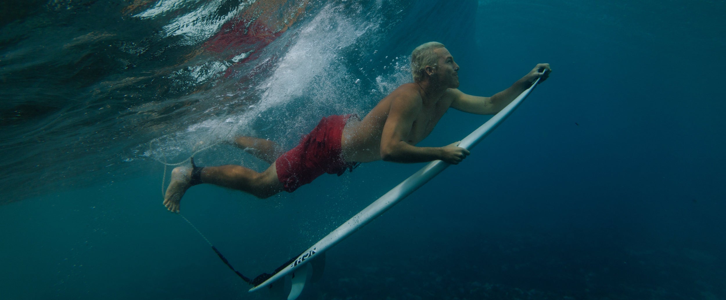 Person paddleboarding underwater with a large wave in the background