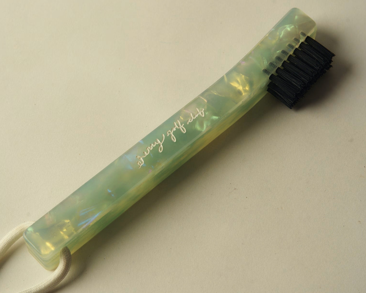 A long-handled cleaning brush with a translucent pale green handle, black bristles, and a white cord loop, photographed on a plain light beige background. The handle is printed with the words 'stay soft lady'.