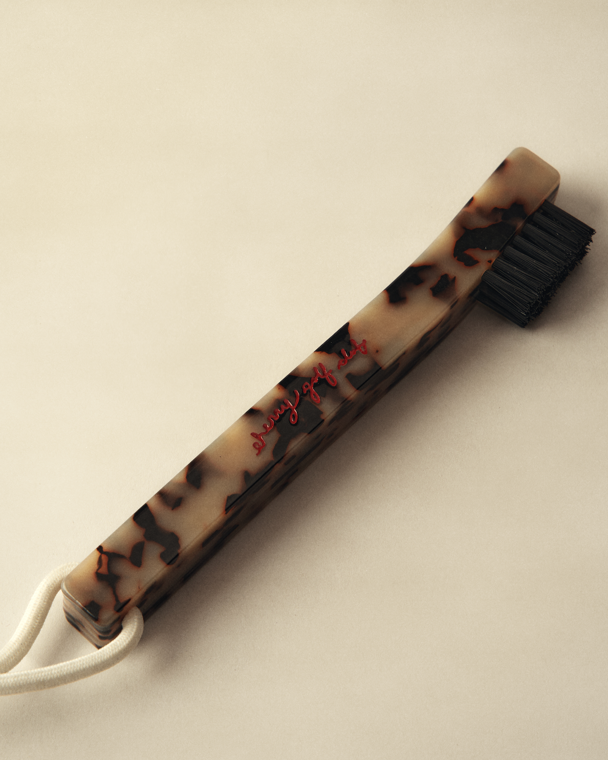 A vintage-style hair bristle brush with a tortoiseshell-patterned handle, black bristles, and a white cord loop, photographed on a warm beige background.