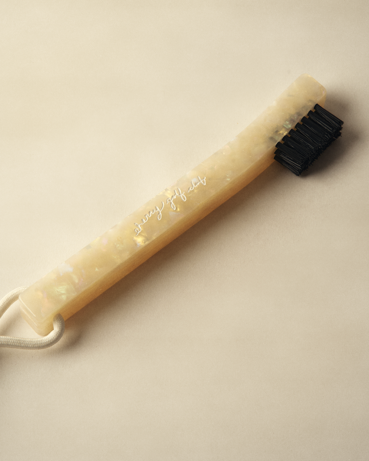 A silicone neck brush with a translucent beige handle featuring iridescent flecks, a black bristle head, and a white drawstring, shown on a neutral beige background.