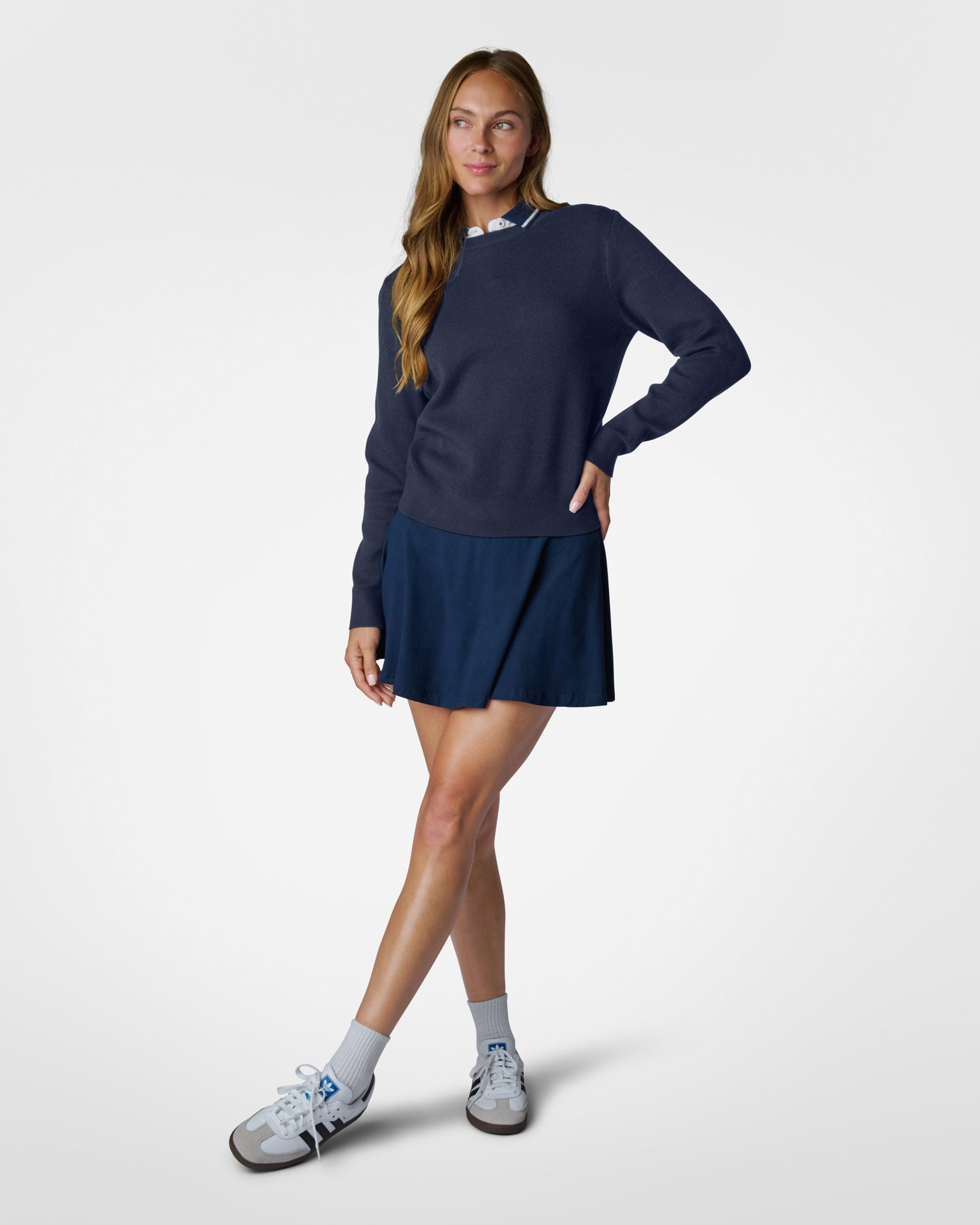 Woman wearing a navy long-sleeve top and skirt with white sneakers on a light gray background