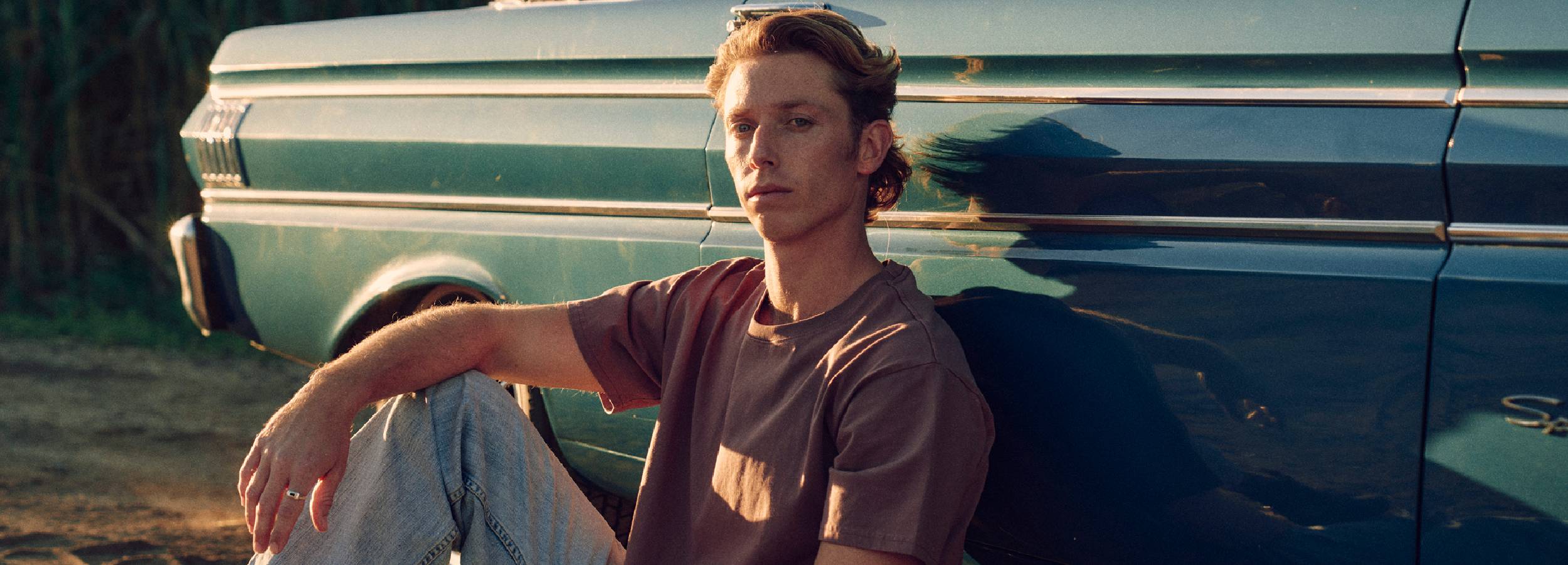 Man sitting against a vintage truck in a natural setting