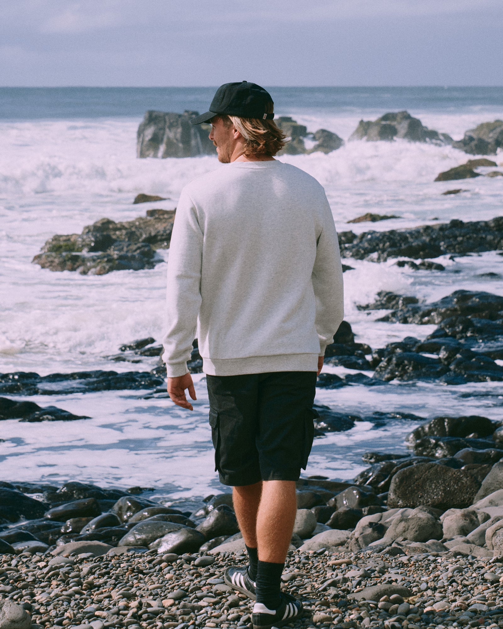 Person walking along a rocky beach with ocean waves in the background