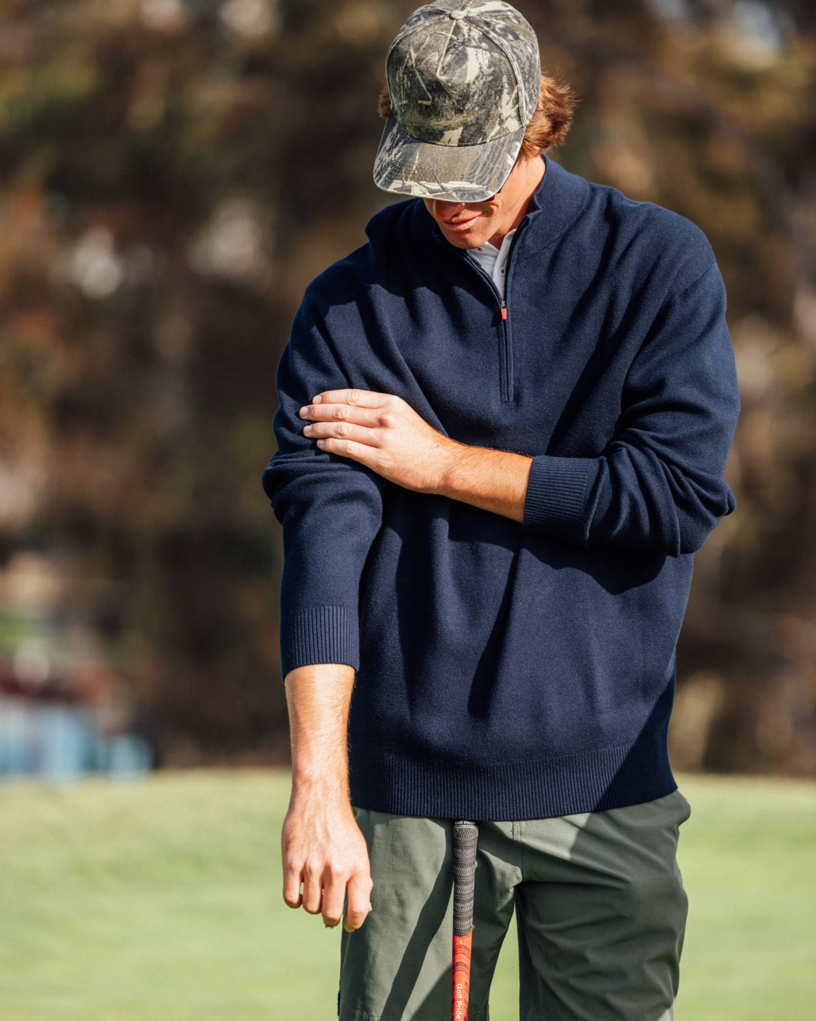 Person wearing a navy sweater and camouflage cap on a golf course