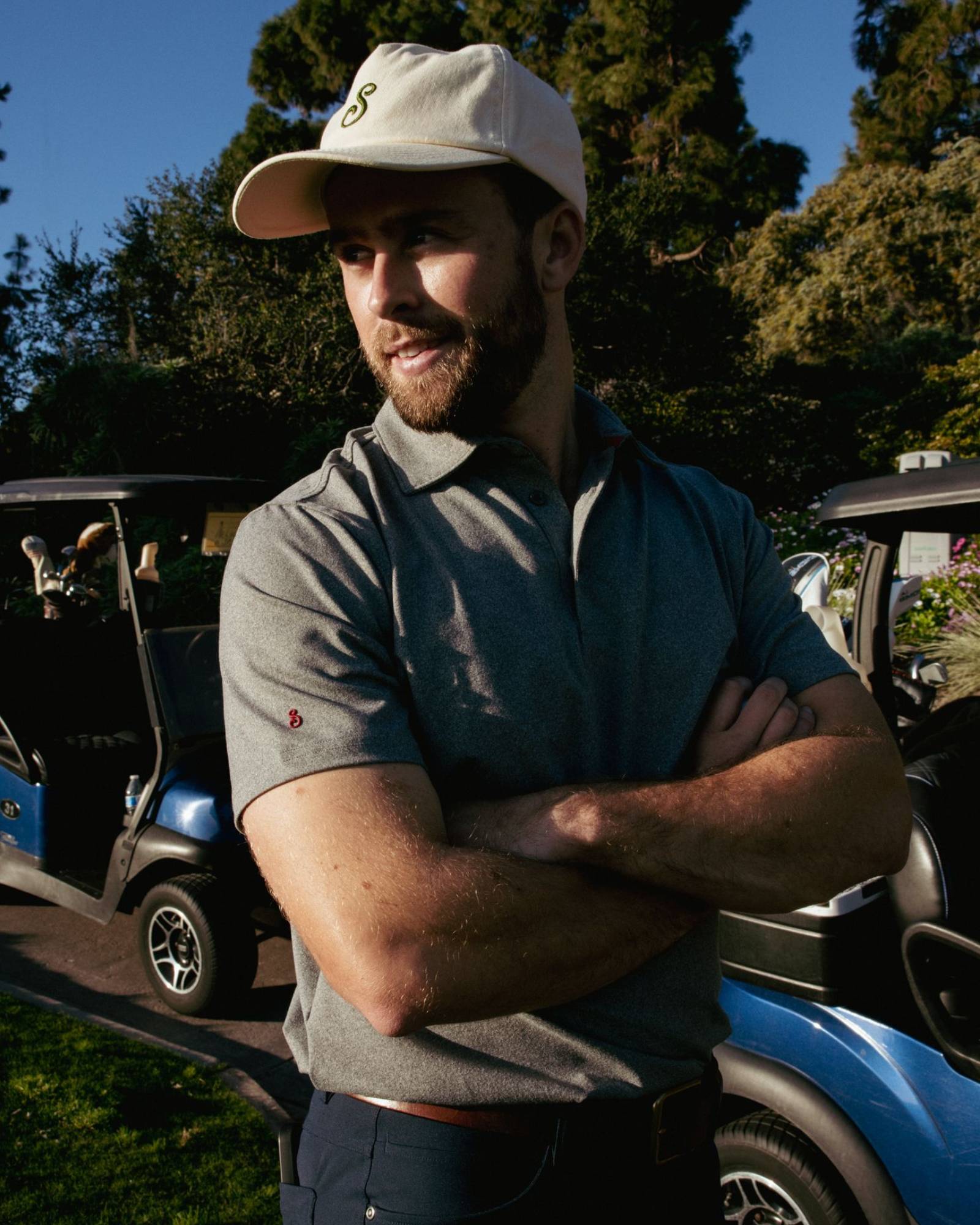 Man standing in front of golf carts wearing a cap and polo shirt, with trees in the background