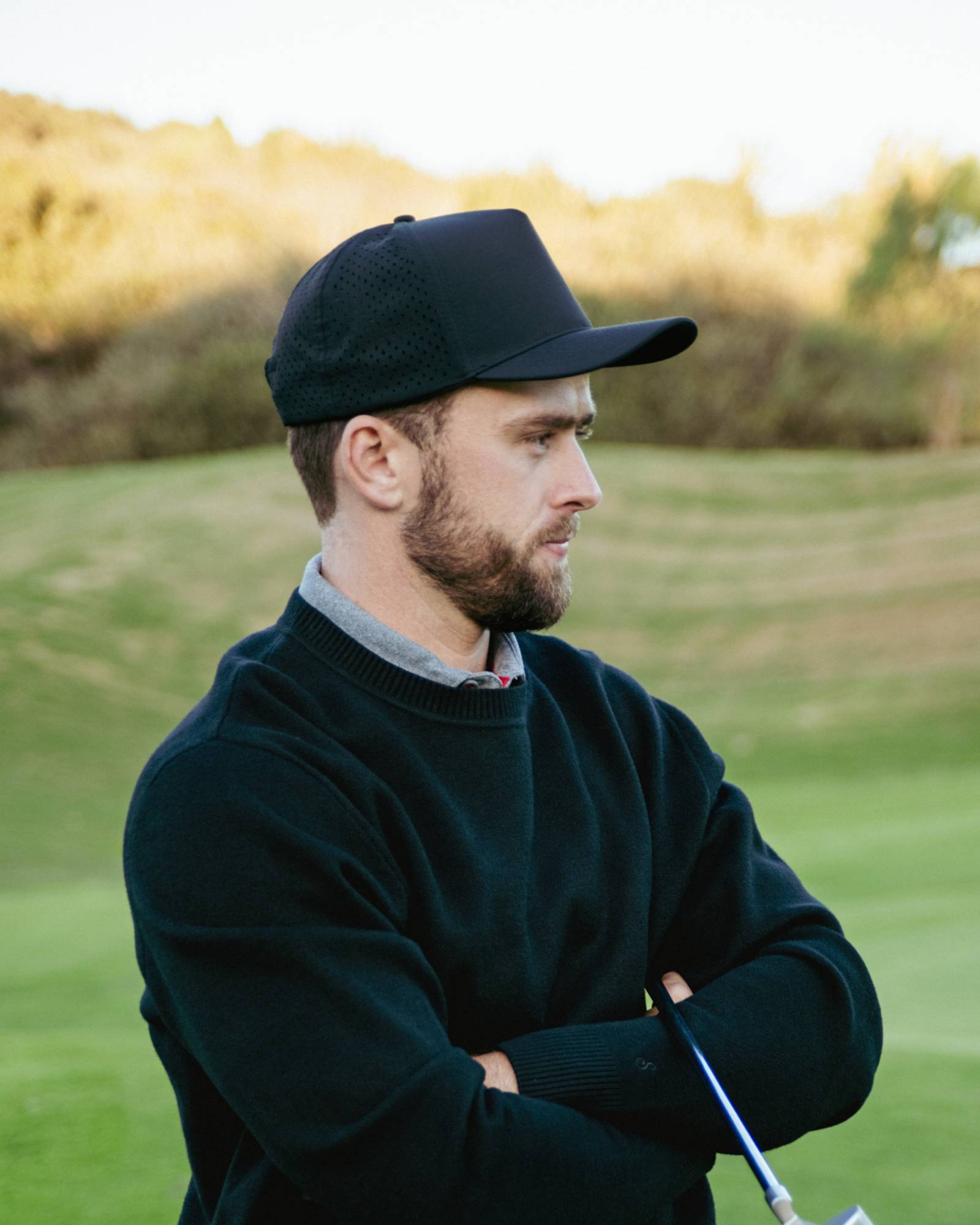 Man in black cap and sweater holding a golf club on a golf course
