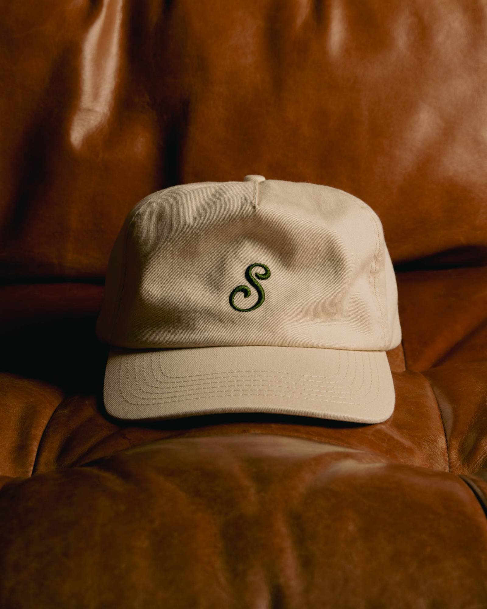 Beige cap with a green logo on a brown leather surface