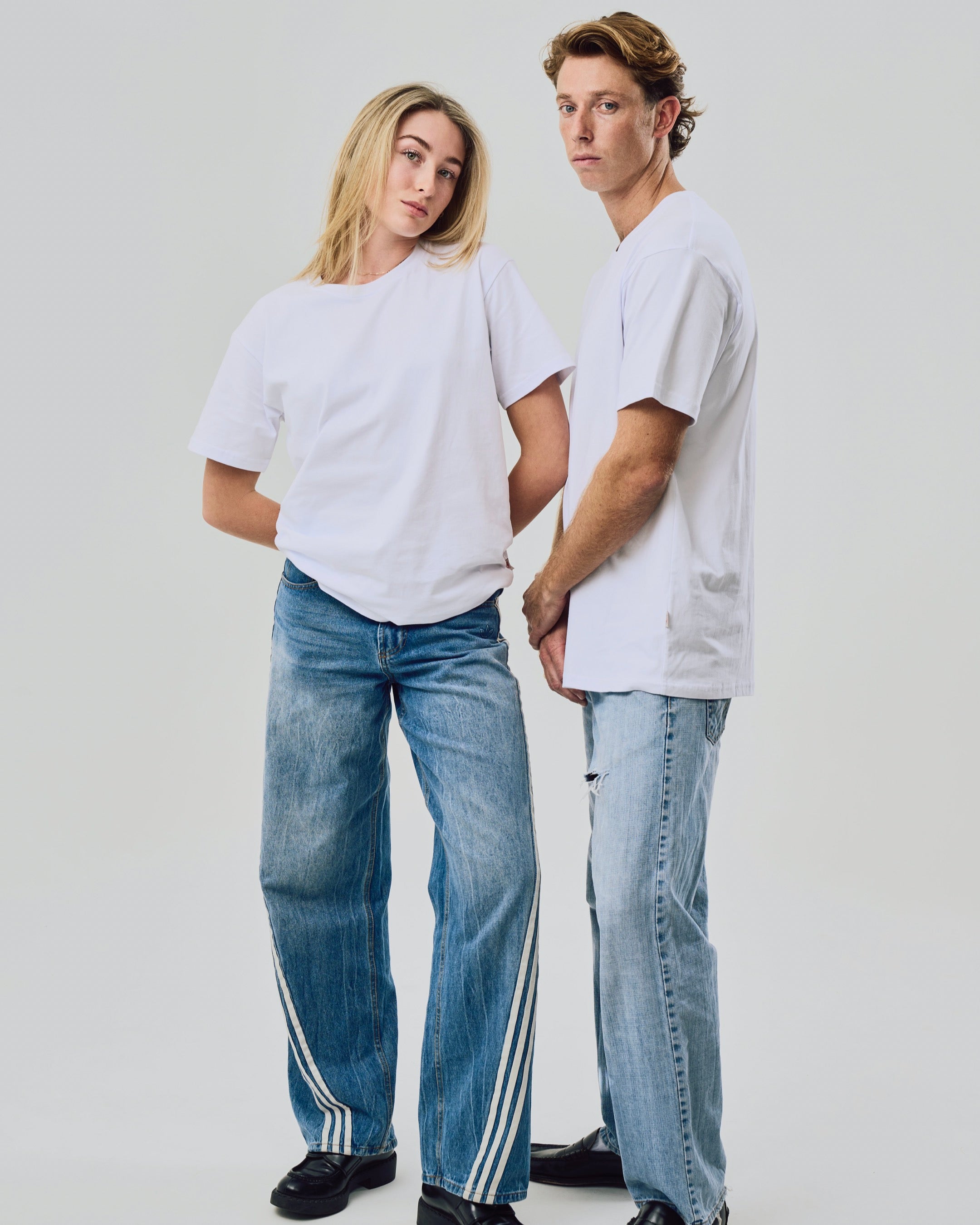 Two people wearing white t-shirts and blue jeans against a plain background