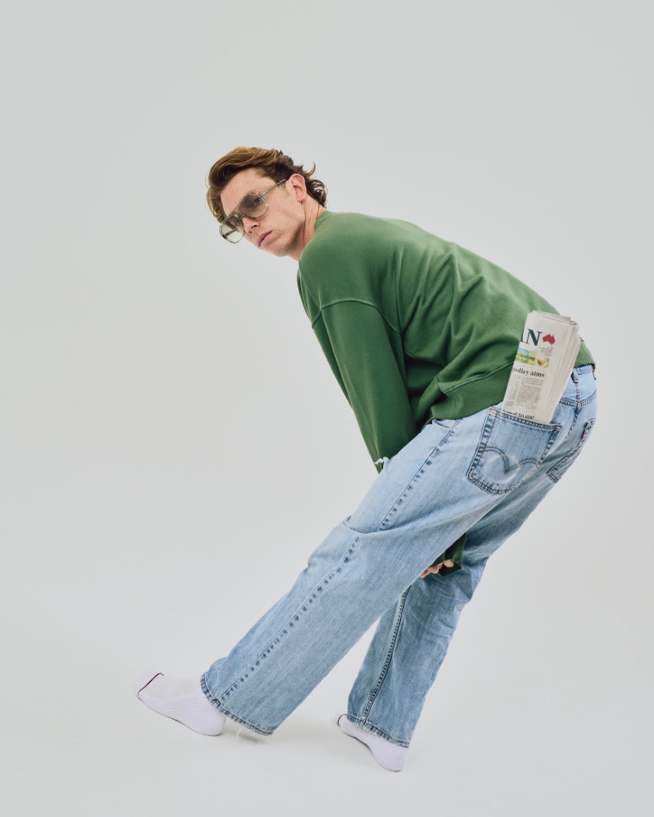 Person wearing a green sweater and light blue jeans with a white background