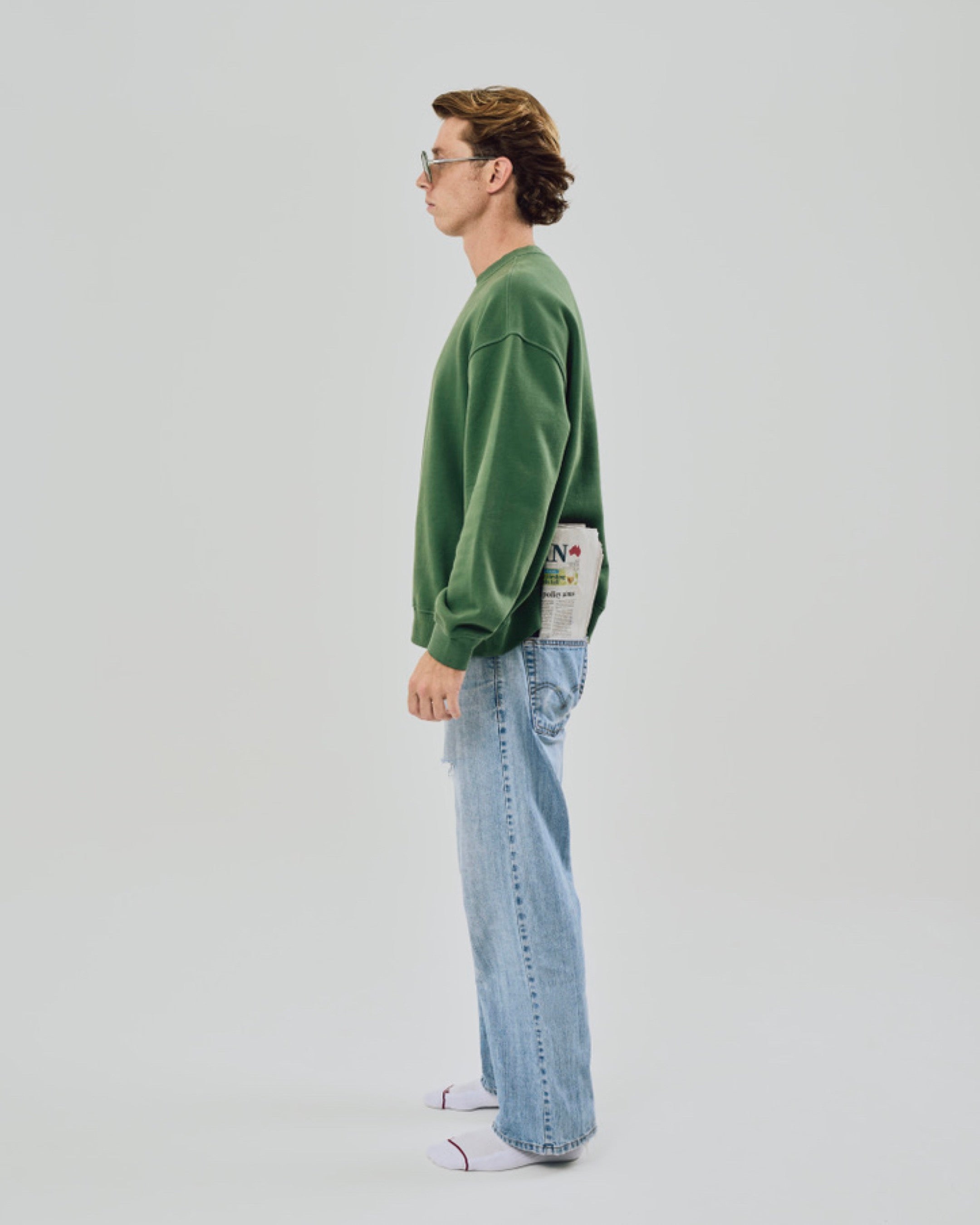 Person wearing a green sweater and light blue jeans on a plain background