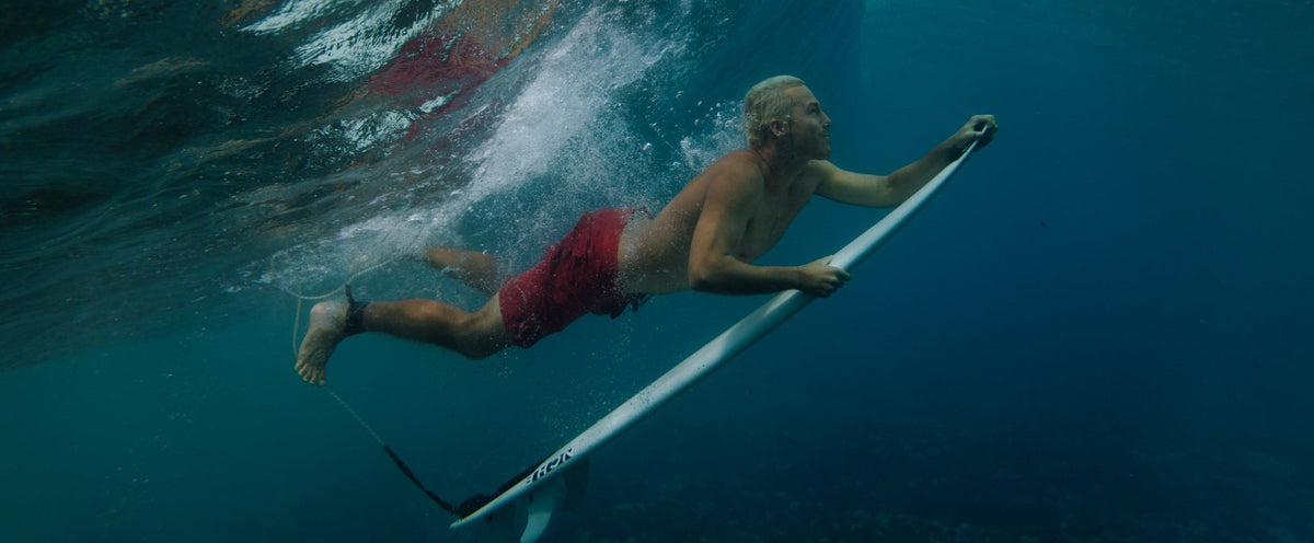 Person paddleboarding underwater with a large wave in the background