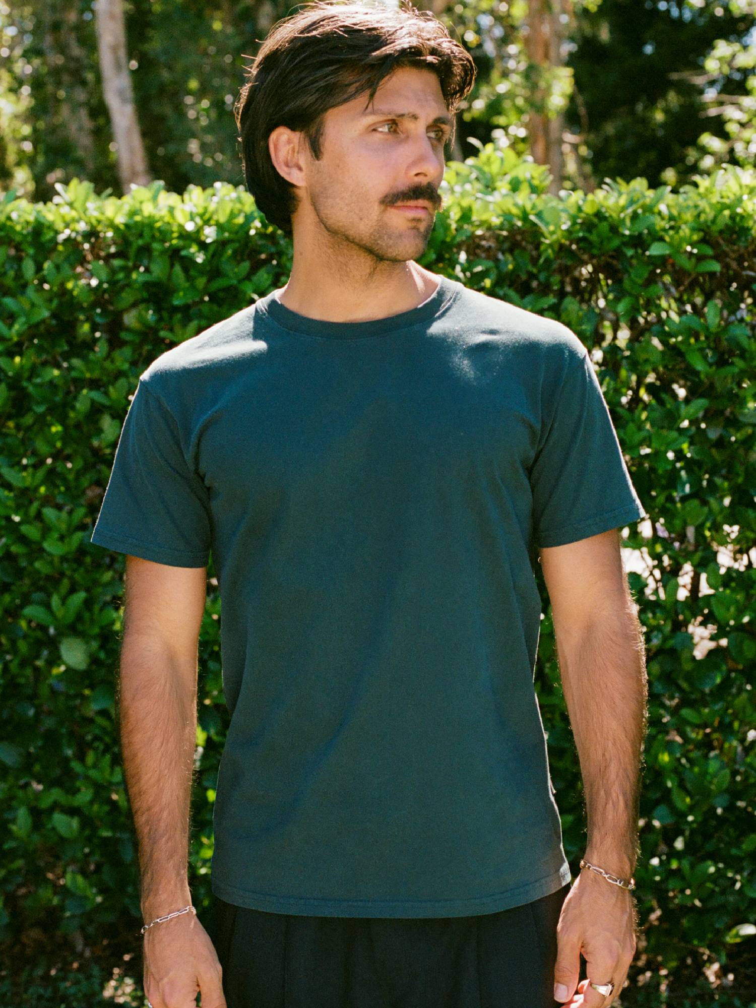 Man wearing green t-shirt with greenery in background 
