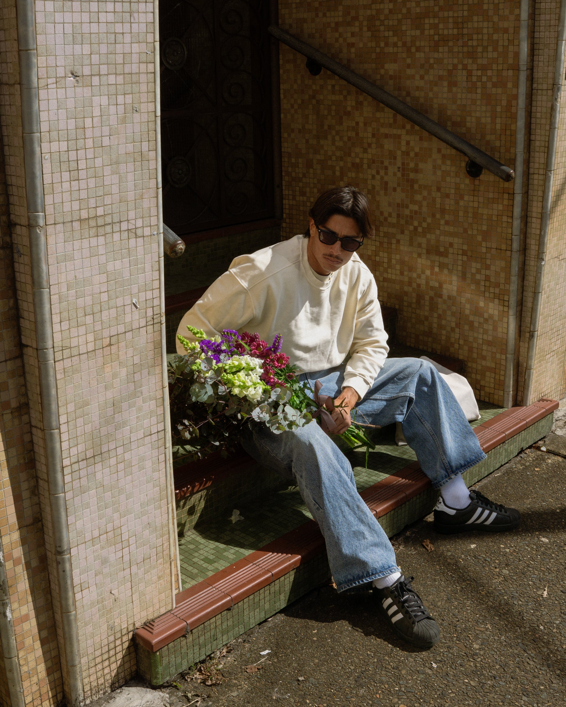 Person sitting on a bench with flowers, wearing sunglasses and casual clothing.