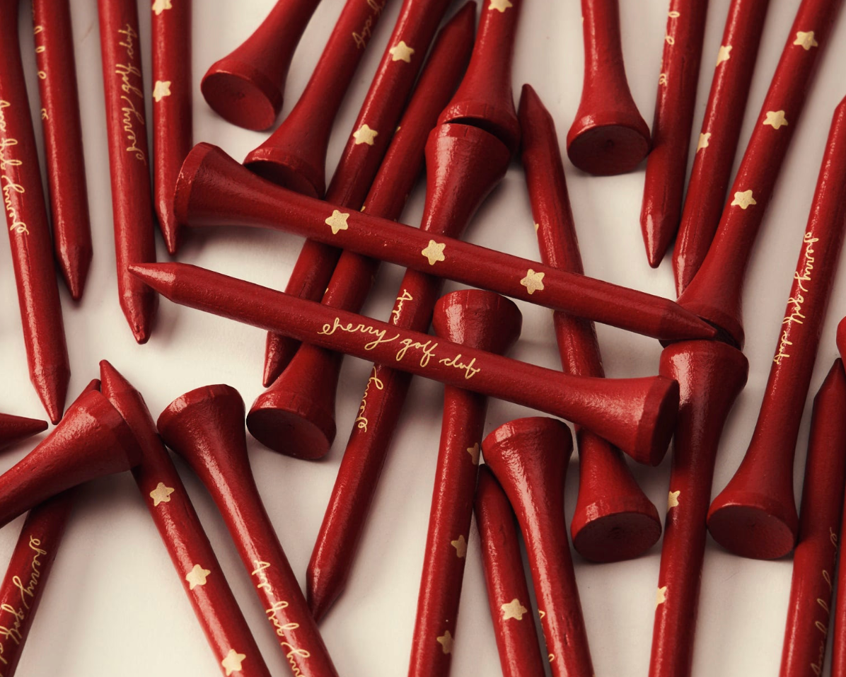 A pile of red wooden golf tees with gold star and script lettering, arranged on a white background.