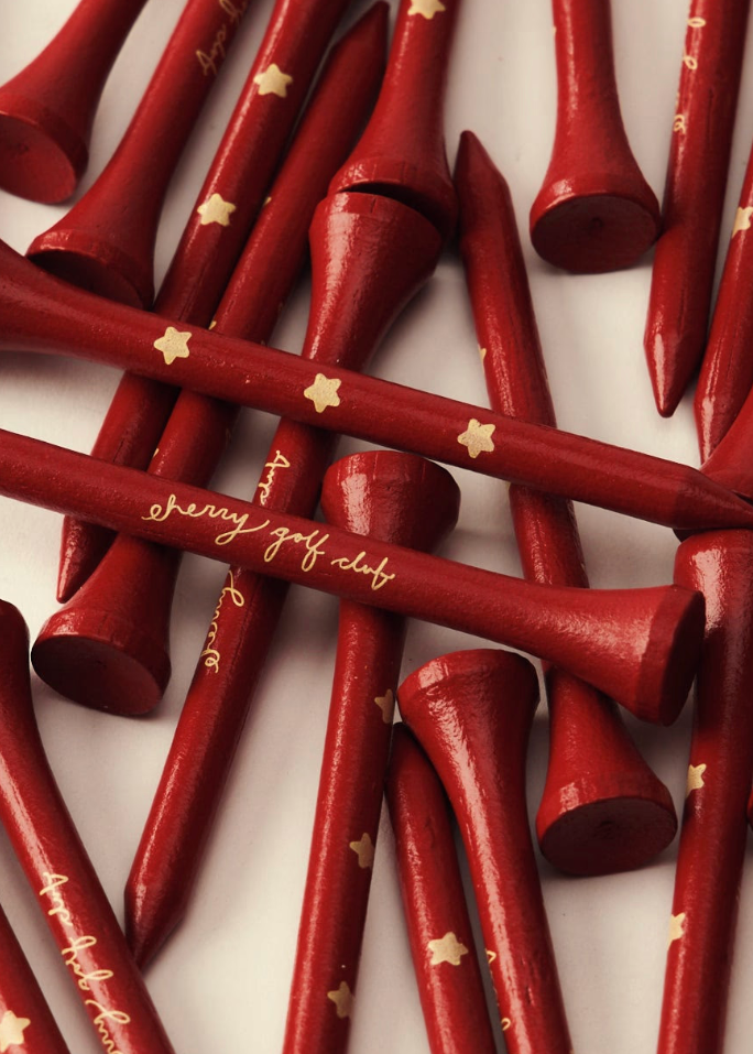 A pile of red wooden golf tees with gold star and script lettering, arranged on a white background.
