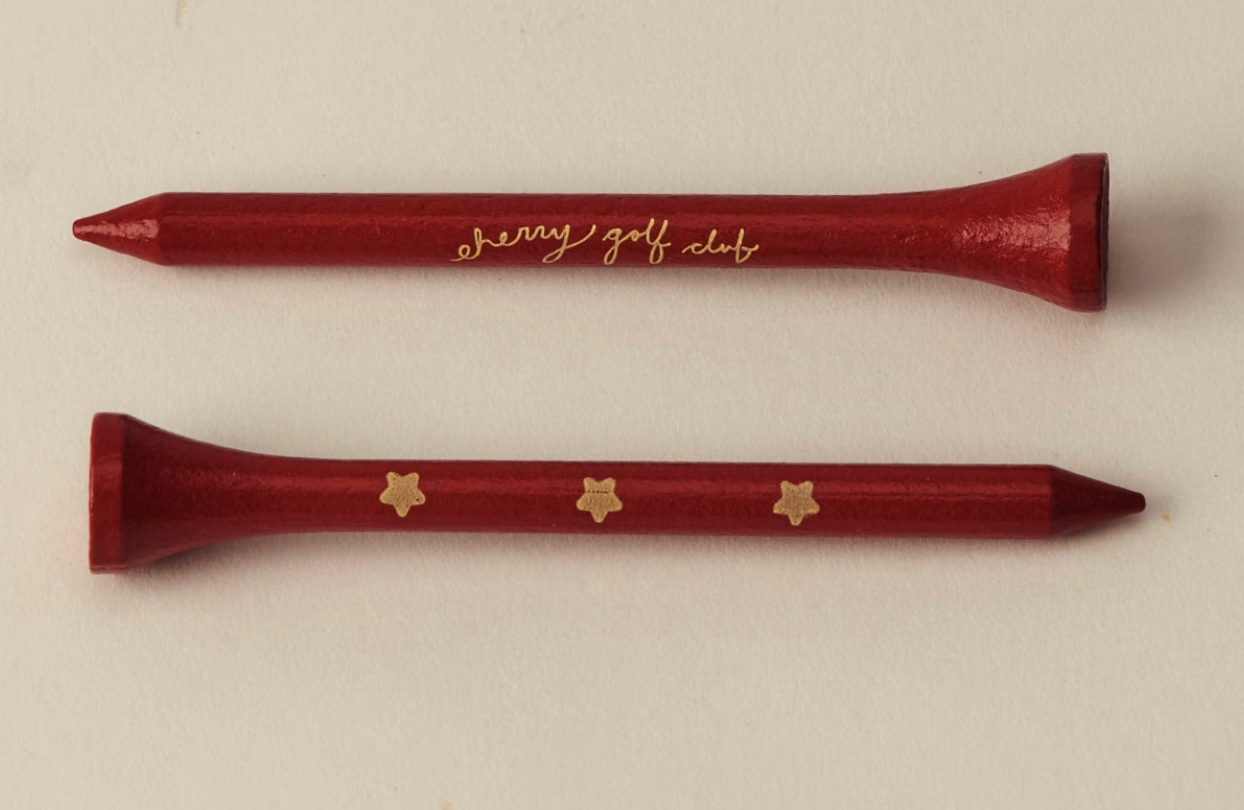 Two red wooden golf tees on a light beige background, one with gold cursive 'benny golf club' lettering and the other with three gold star-like logos.