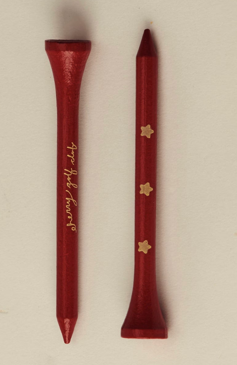 Two red wooden golf tees on a light beige background, one with gold cursive 'benny golf club' lettering and the other with three gold star-like logos.