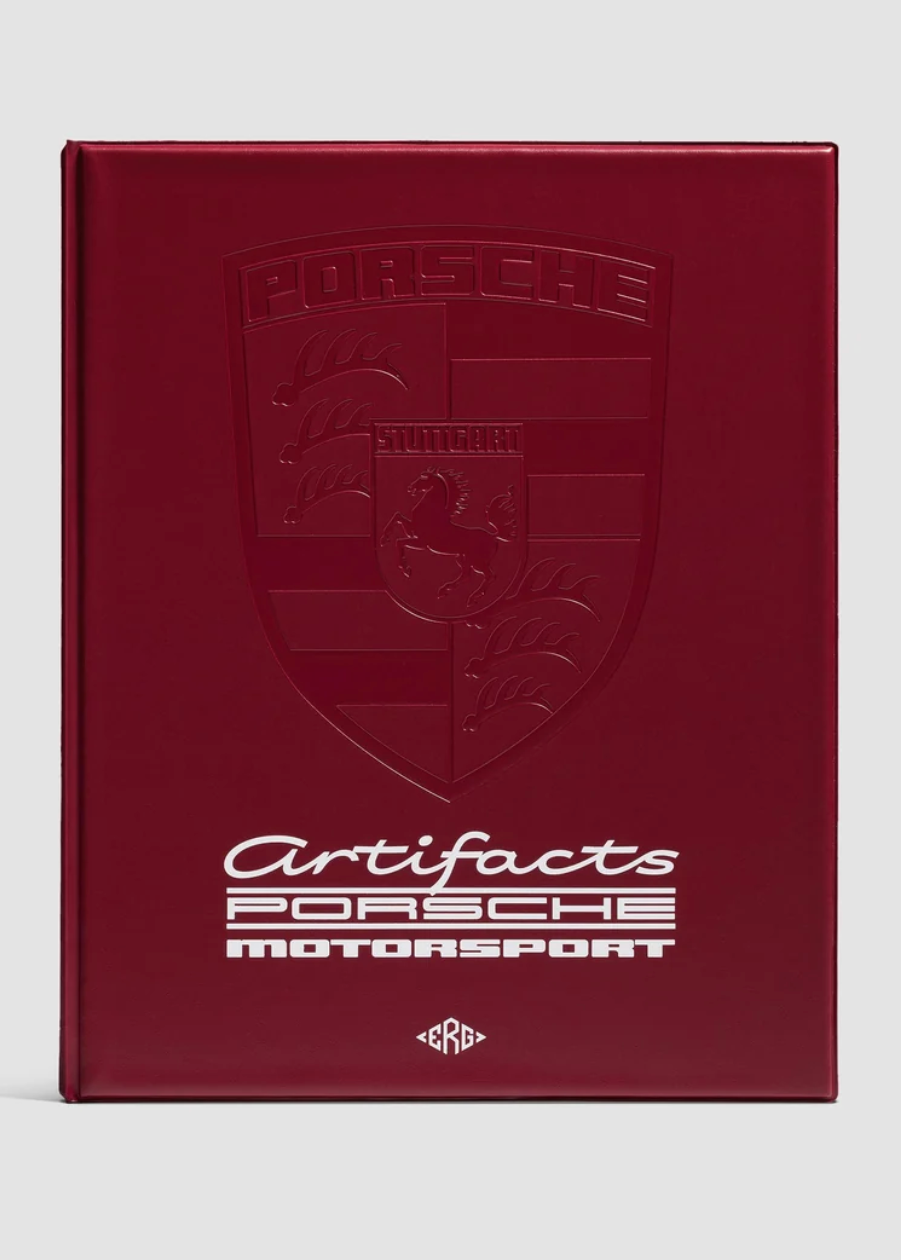A hardcover book or album titled 'Artifacts Porsche Motorsport' with a deep burgundy cover, embossed Porsche crest, and white text, shown on a light gray background.