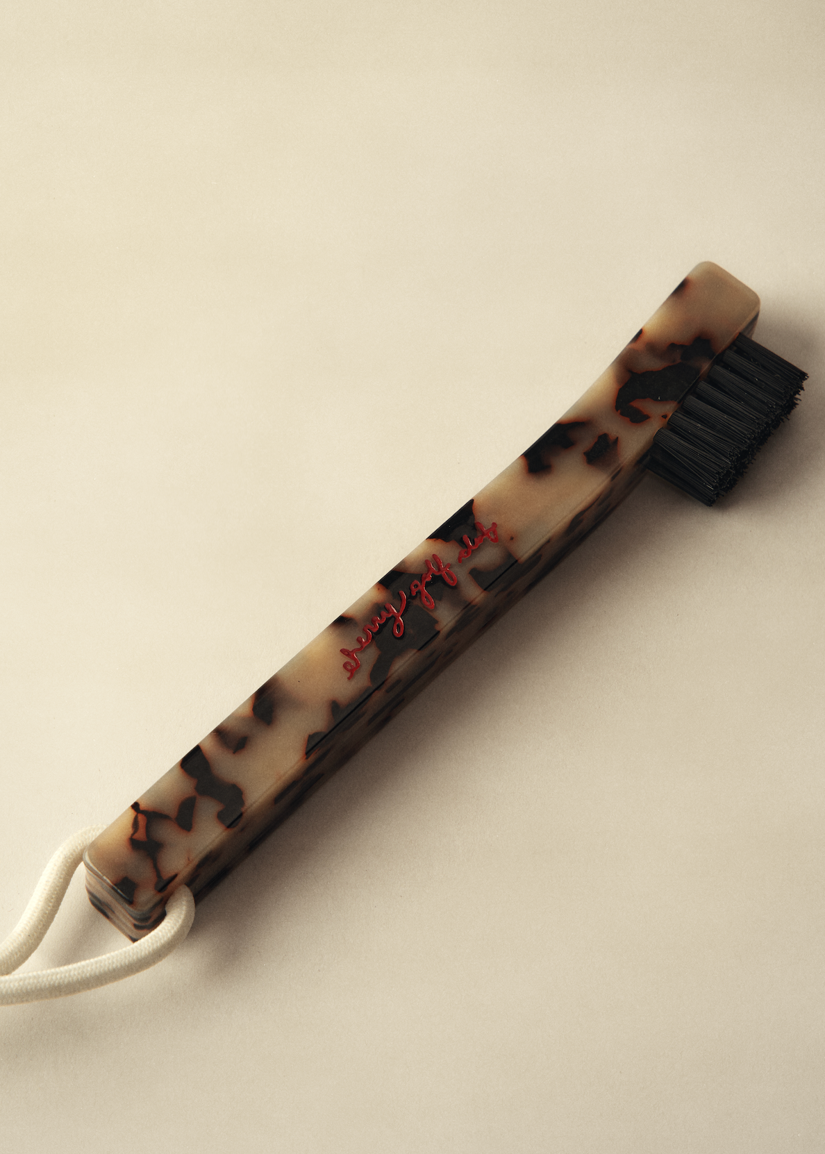 A vintage-style hair bristle brush with a tortoiseshell-patterned handle, black bristles, and a white cord loop, photographed on a warm beige background.