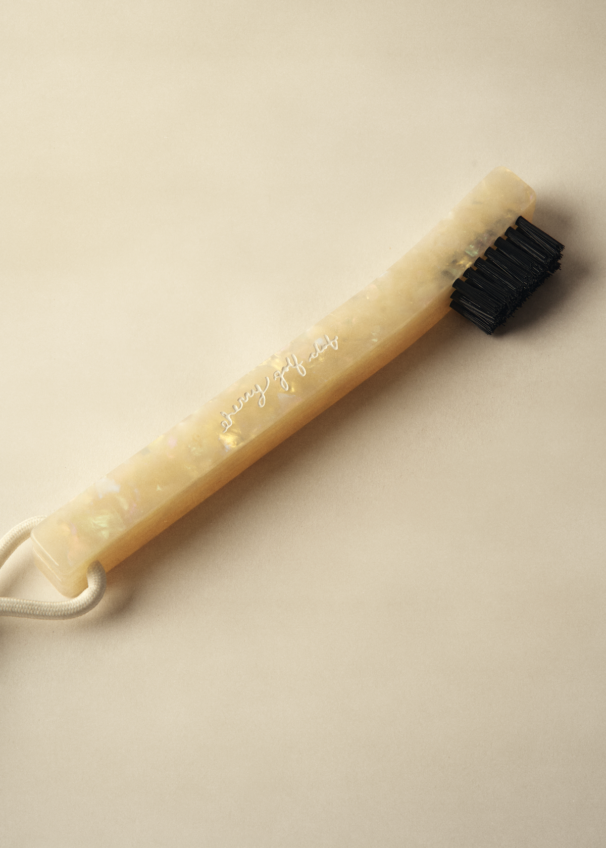 A silicone neck brush with a translucent beige handle featuring iridescent flecks, a black bristle head, and a white drawstring, shown on a neutral beige background.