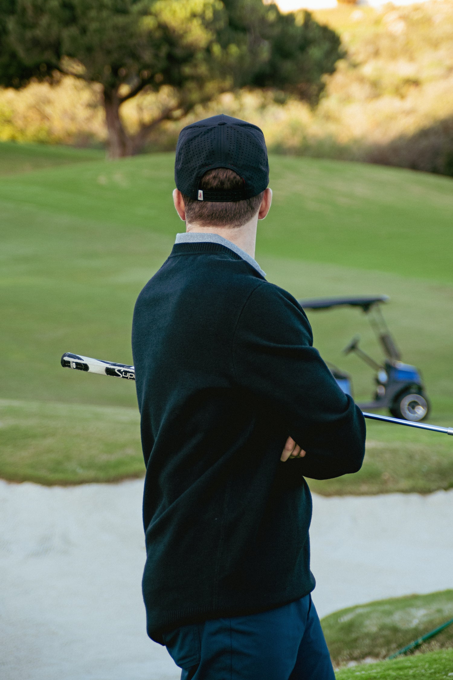 Man in dark clothing holding a golf club on a golf course with a blurred background