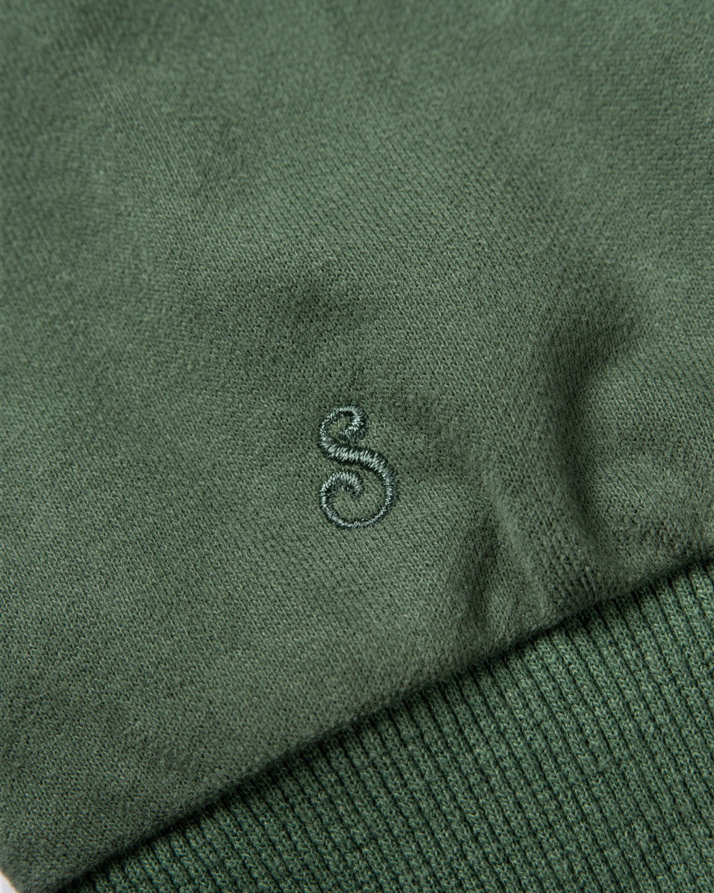Close-up of a green sweater with a small embroidered logo on the sleeve.