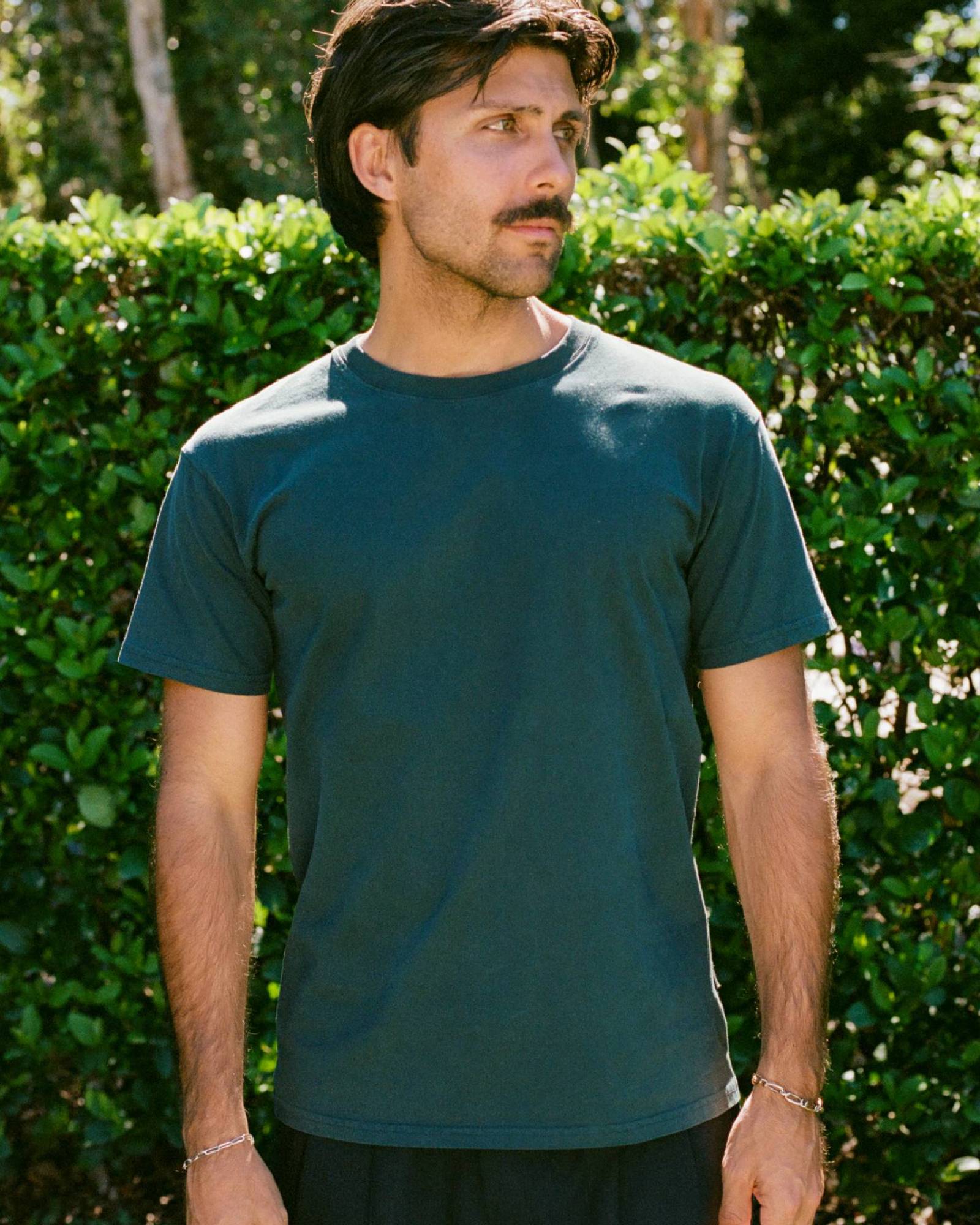 Man wearing a green t-shirt standing in front of green foliage