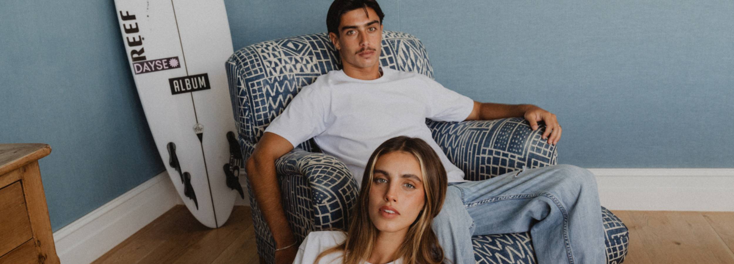 Man and woman sitting on a couch with a surfboard in the background