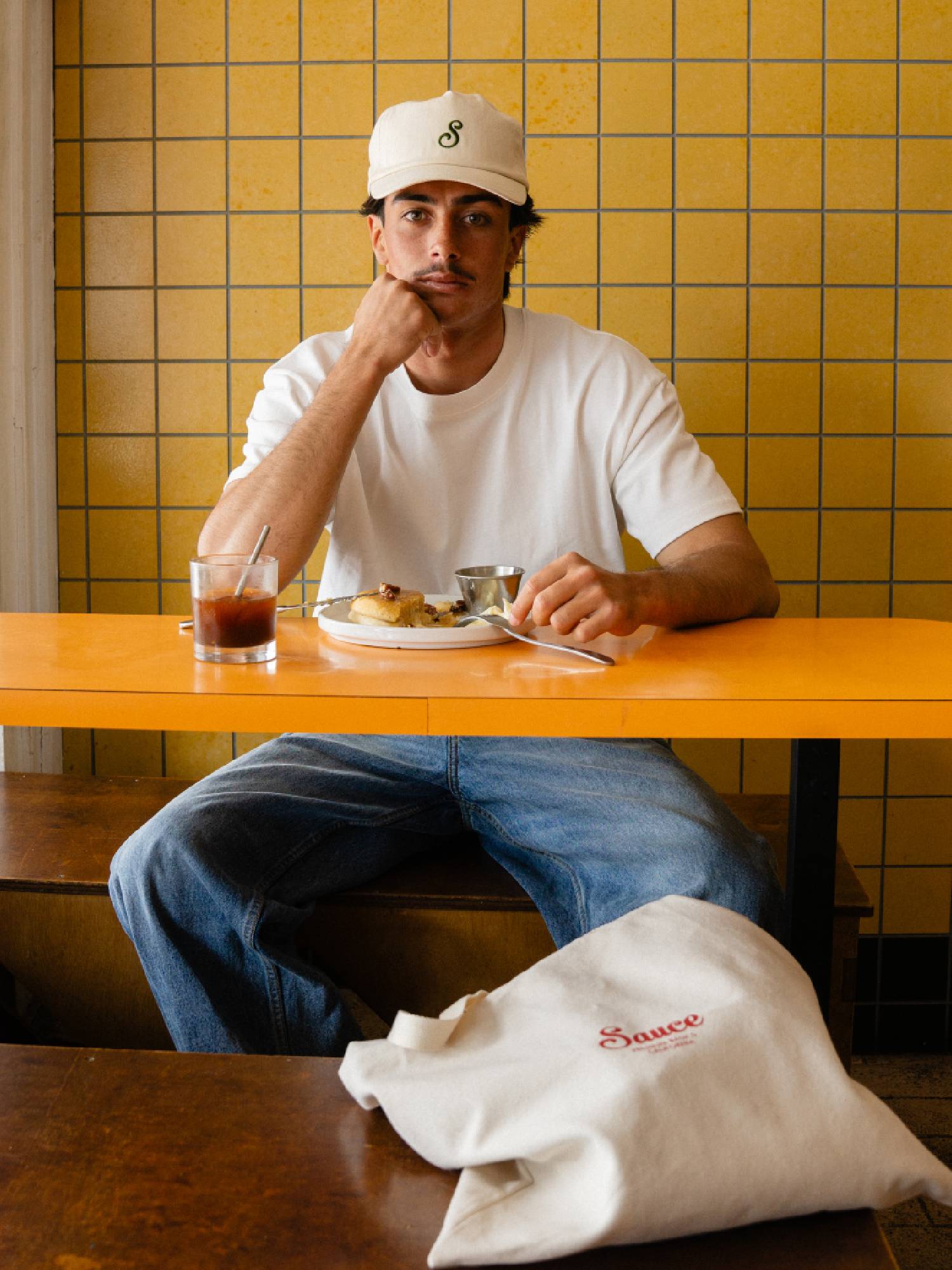 Man wearing white t-shirt and off white cap against yellow tiled background 