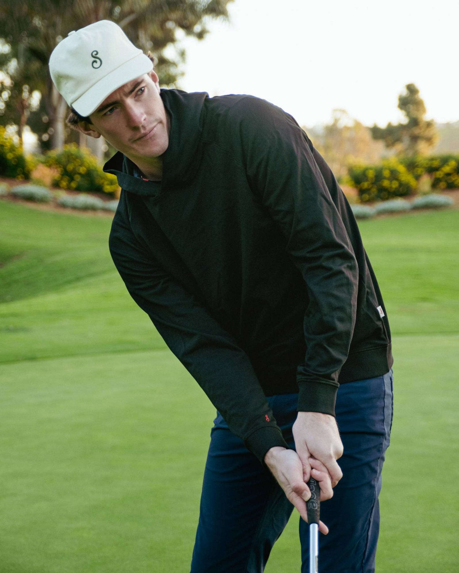 Man in black hoodie and white cap playing golf on a green court