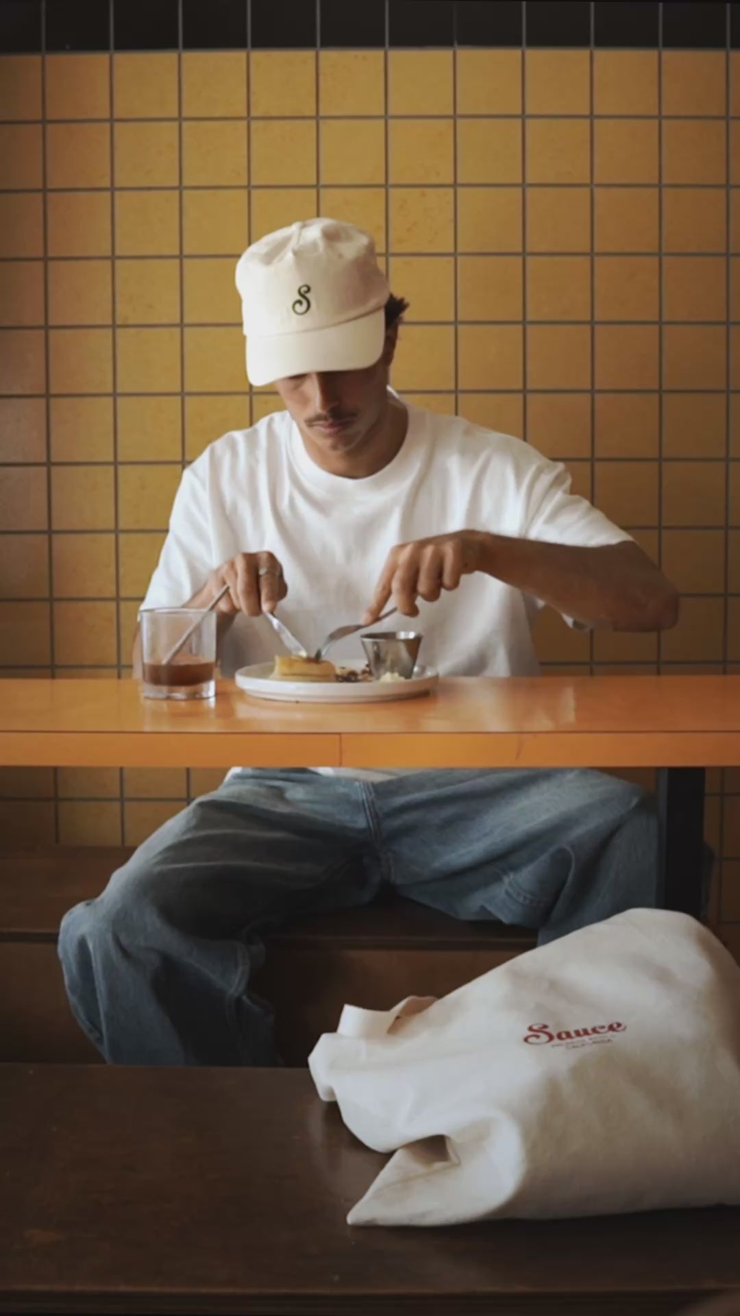 Person eating food wearing a white t-shirt and off white cap with a yellow tiled background