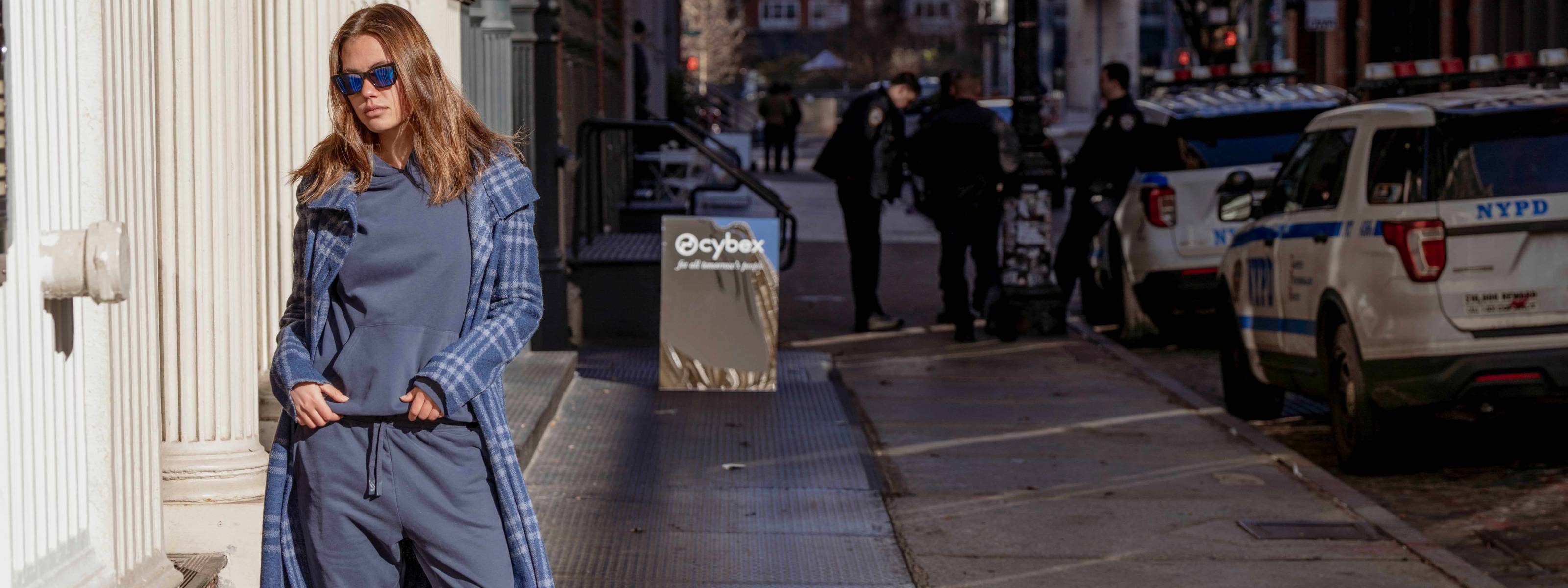 Woman in a blue outfit standing on a city street with police cars in the background